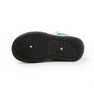 Black rubber sole of a baby sneaker with textured grip and white upper showing blue and red accents