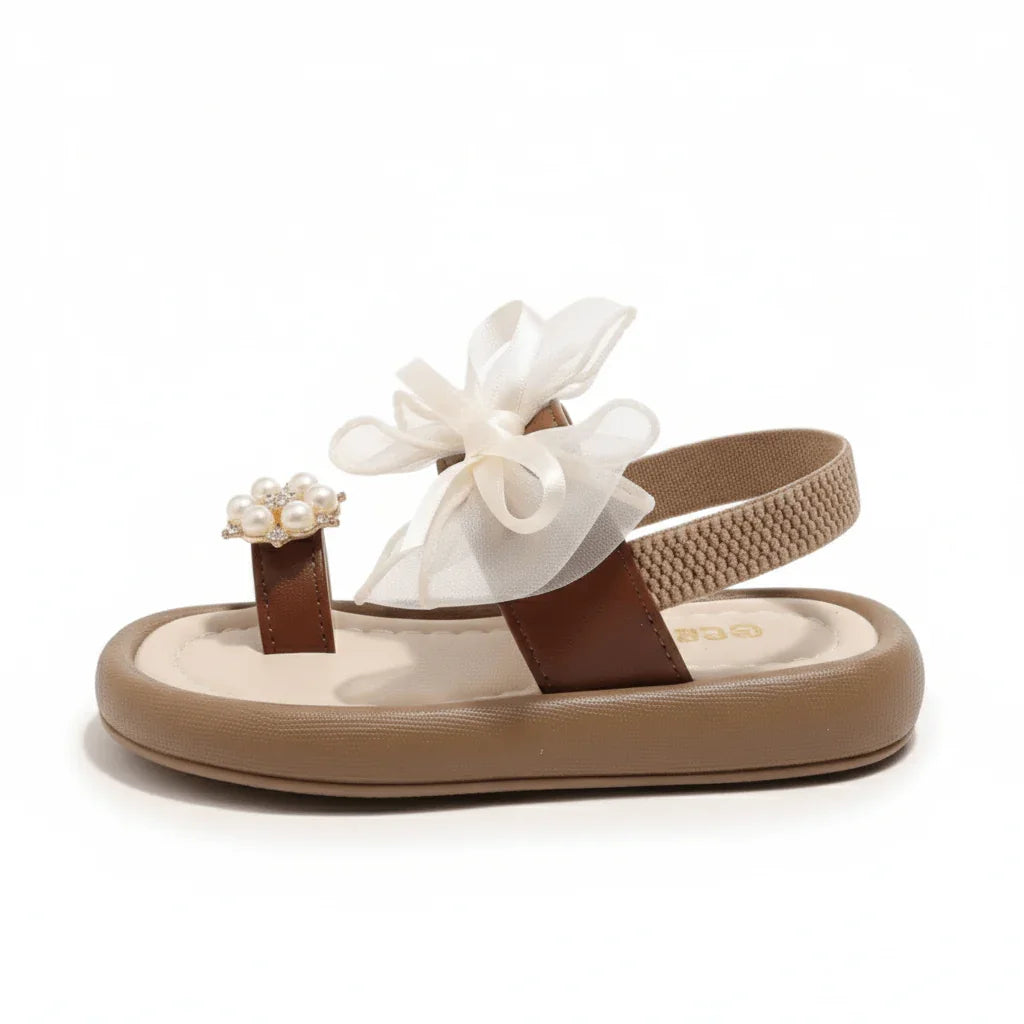 Brown toddler sandal with cushioned sole, pearl toe ring, and white ribbon bow accent