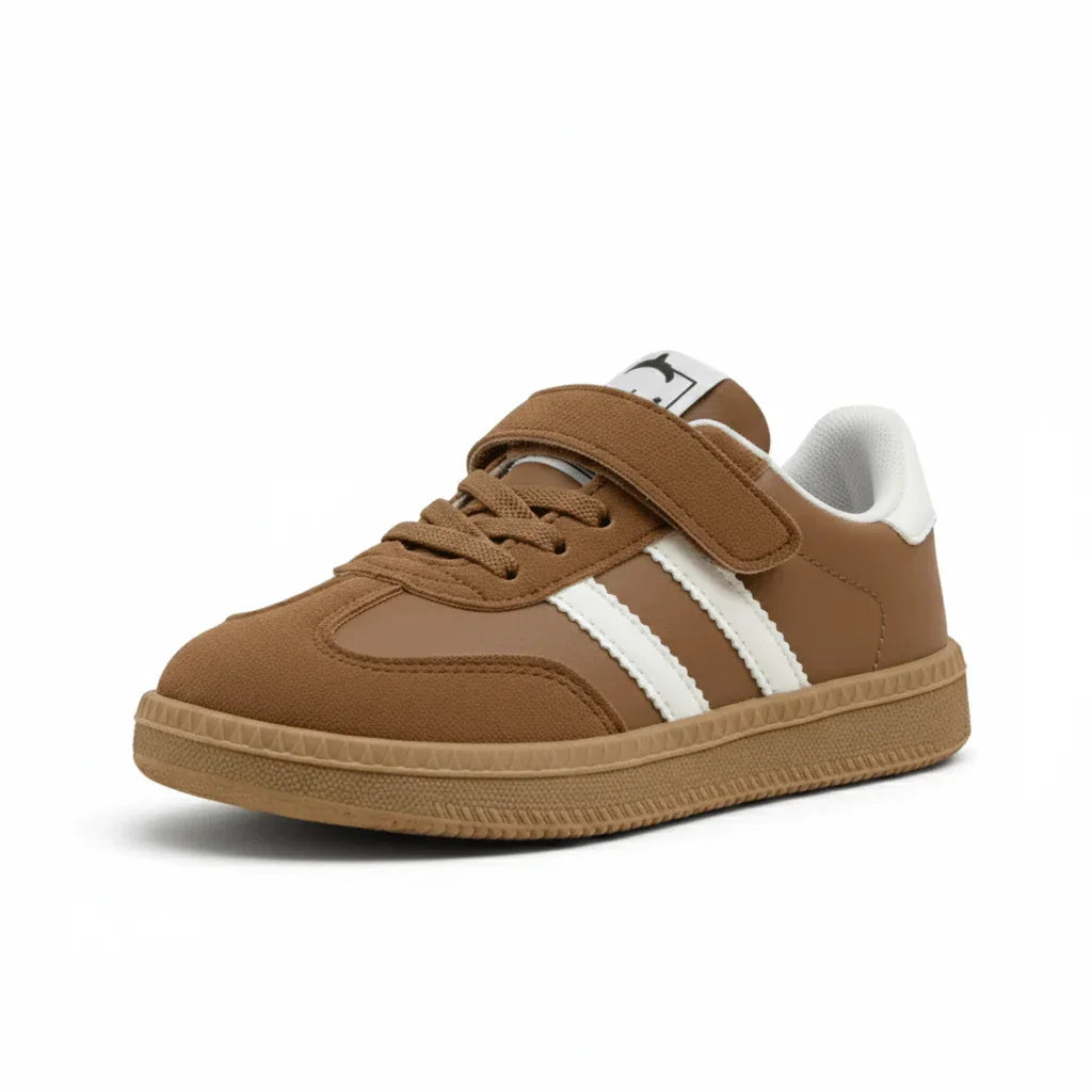 Classic brown kids sneaker with white stripes, lace-up and Velcro strap on white background